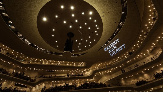 Szene aus der Opening Night 2019 des NDR Elbphilharmonie Orchesters: Der beleuchtete Zuschauerraum der Elbphilharmonie mit einer Projektion "#KLINGTnachGILBERT" an der Decke des Großen Saales © NDR Foto: Peter Hundert