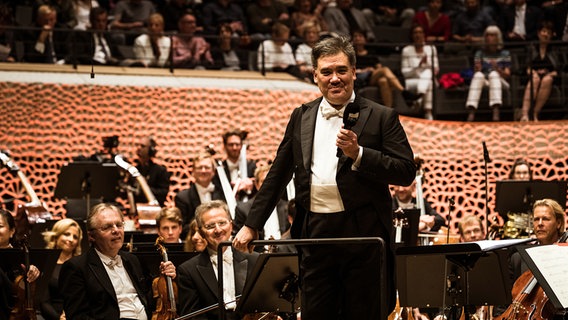 Szene aus der Opening Night 2019 des NDR Elbphilharmonie Orchesters: Alan Gilbert mit Mikrofon in der Hand am Dirigentenpult im Großen Saal der Elbphilharmonie © NDR Foto: Peter Hundert