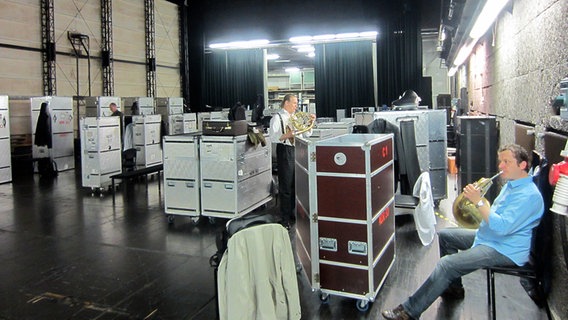 Backstage-Szene: Zwei Hornisten spielen sich zwischen den Instrumenten-Cases auf ihren Instrumenten ein. © NDR Sinfonieorchester 