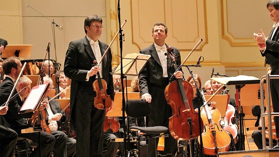 Applausszene: Stefan Wagner und Andreas Grünkorn auf der Bühne der Laeiszhalle. Rechts am Bildrand applaudiert Dirigent Alan Gilbert. © NDR Foto: Kristien Daled