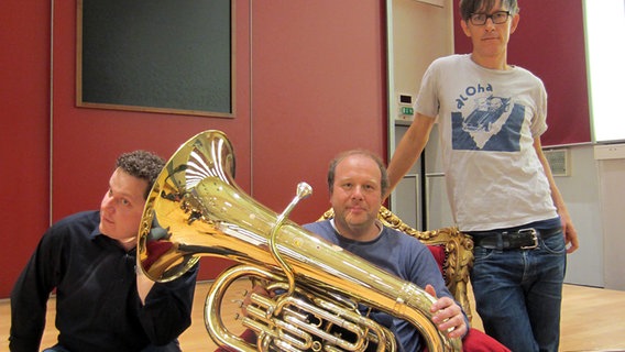 Tubist Markus Hötzel auf einem Thron sitzend, Dave Claessen lauscht in das Instrument hinein, rechts neben dem Thron steht Jörg Kleemann © NDR 