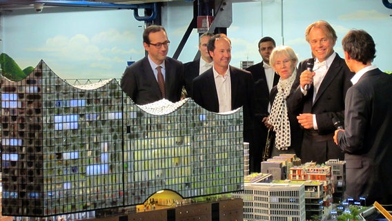 Christoph Lieben-Seutter, Frederik Braun, Barbara Kisseler und Thomas Hengelbrock (v.l.n.r.) stehen hinter dem Miniatur Wunderland-Modell der Elbphilharmonie. © NDR Foto: Markus Hötzel
