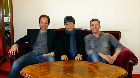 Jeroen Berwaerts, Toshio Hosokawa und Matthias Pintsche auf einem roten Sofa nebeneinander sitzend. © NDR 