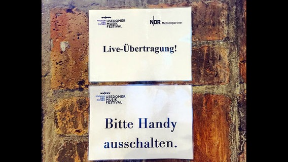 Schilder auf der Wand mit der Aufschrift "Live-Übertragung, Bitte Handy ausschalten."  