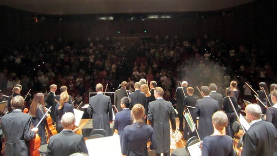 Blick über die stehenden Orchestermusiker ins Publikum © NDR SO 