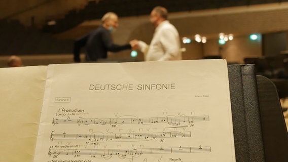 Screenshot: Blick auf eine Notenstimme für Eislers "Deutsche Sinfonie", dahinter geben sich Carlos Miguel Prieto und Matthias Goerne einen "fist bump" © NDR Foto: Screenshot
