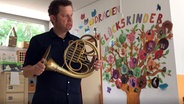 Screenshot: Hornist Dave Claessen vom NDR EO steht mit seinem Instrument in der Hand in einem leeren Kindergarten © NDR Foto: Screenshot