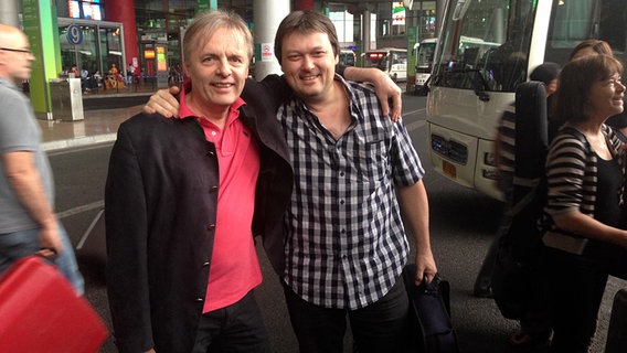 Roland Greutter und Stephen Sitarski Arm in Arm vorm Flughafengebäude Roland Greutter und Stephen Sitarski Arm in Arm vorm Flughafengebäude © NDR Sinfonieorchester