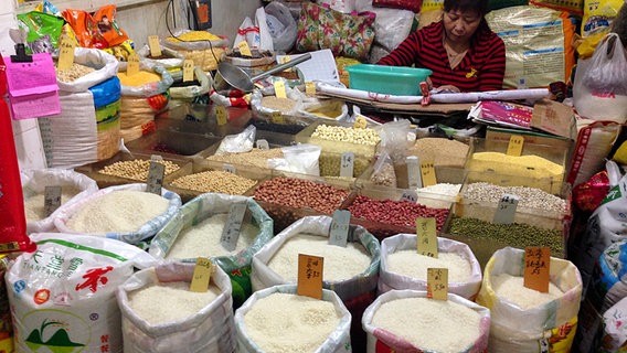 Frau hinter einem Verkaufsstand mit vielen Säcken voll Bohnen und Reis  