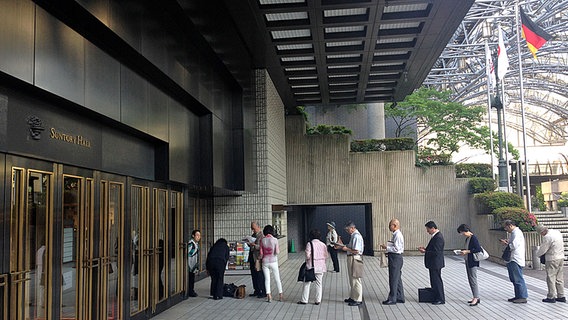 Besucher stehen in einer Schlange vor der Suntory Hall in Tokio an  