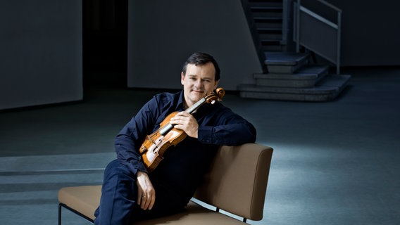 Der Geiger Frank Peter Zimmermann auf einer Bank sitzend mit seinem Instrument. © Irène Zandel Foto: Irène Zandel