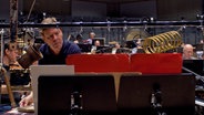Screenshot: Magnus Lindberg steht hinter einem Notenständer und Klangobjekten. © NDR 