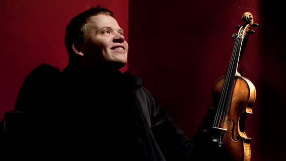 Porträt vor roter Wand: Pekka Kuusisto mit seiner Geige © Maija Tammi 