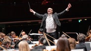 Ein Dirigent steht mit erhobenen Armen vor einem Orchester. Es ist Andrew Manze. © NDR Foto: MIchael Neugebauer