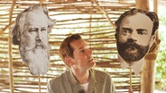 Malte Arkona betrachtet Fotografien von Brahms (links) und Dvořák (rechts) © NDR 