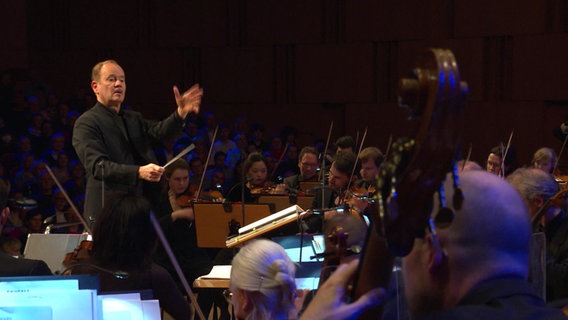 Dirigent Frank Strobel steht vor der NDR Radiophilharmonie und dirigiert. © NDR 