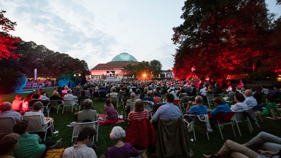 Ein Mann prostet vor Beginn des "Hannover Proms"-Konzerts mit einer Frau neben sich auf der Picknickdecke auf den Abend an. © NDR Foto: Julius Matuschik