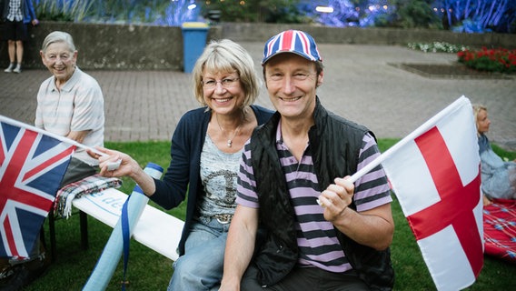 Susanne (li.) und Rüdiger (re.) warten auf den Beginn von "Hannover Proms" 2016 und halten dabei jeweils eine Großbritannien- und eine England-Flagge in der Hand. © NDR Foto: Julius Matuschik