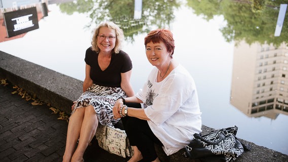 Bärbel (li.) und Marion (re.) warten sitzen vor Beginn des "Hannover Proms"-Konzerts gemeinsam am Wasser. © NDR Foto: Julius Matuschik