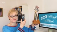 Teaserbild für die Folge "Metronom" des Zwergen-Musiklexikons mit Frau Grünig, die zwei Metronome in den Händen hält © NDR 