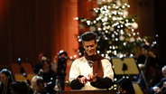 Matthias Keller vor einem Pult in der Luft wie auf einer Schreibmaschine tippend spricht Cratchit, die Geister der Weihnacht und andere © NDR Foto: Micha Neugebauer