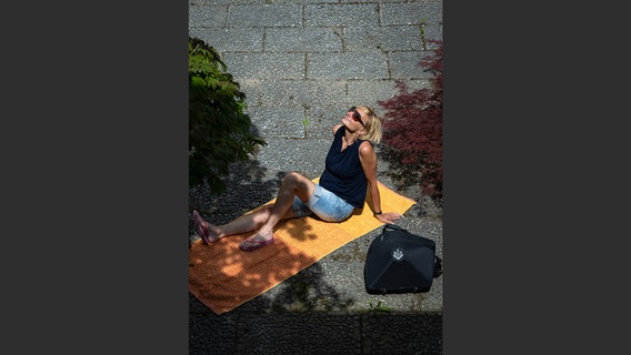Margje Imandt mit Horn-Koffer auf einer gelben Decke in der Sonne © NDR Foto: François Lefèvre