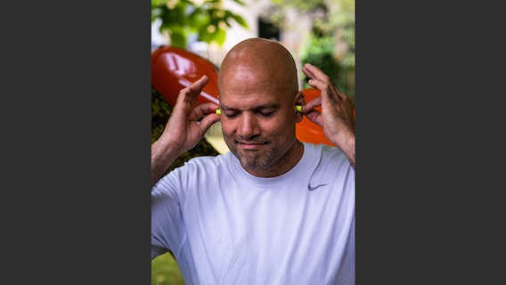 Oliver Mascarenhas steckt sich mit geschlossenen Augen Gehörschutz in die Ohren © NDR Foto: François Lefèvre