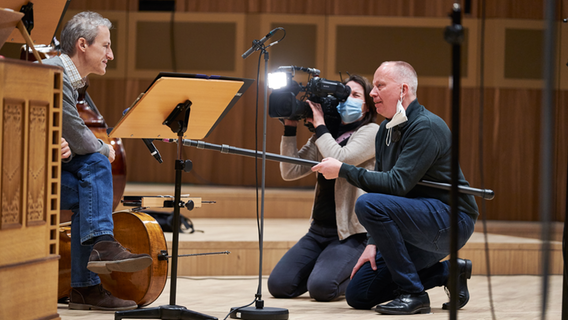 Ein Musiker der NDR Radiophilharmonie im Interview mit einem Fernsehredakteur und einer Kamerafrau © NDR Foto: Micha Neugebauer