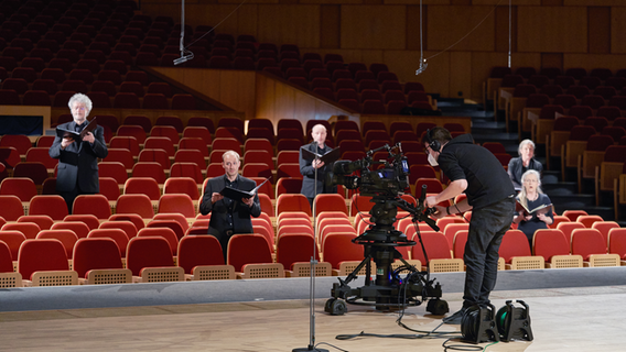 Sänger*innen des NDR Chors im Großen Sendesaal im Landesfunkhaus in Hannover stehend werden von einem Kamerateam abgefilmt © NDR Foto: Micha Neugebauer