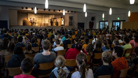 Die Schülerinnen und Schüler der Magister-Nothold-Grundschule Lindhorst sitzen in ihrer Aula. © NDR Foto: Helge Krückeberg