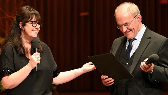 Bratscherin Rebecca Gould steht neben Moderator Friedrich Stenger-Lutz. Beide halten ein Mikrofon in der Hand. © NDR Foto: Carsten P. Schulze