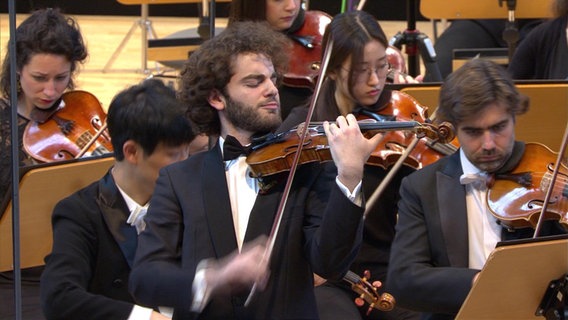 Emmanuel Tjeknavorian spielt Geige. Im Hintergrund das Orchester. © NDR 