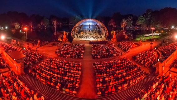 Vor einer rot beleuchteten Open Air Bühne sitzt viel Publikum. © Axel Herzig Foto: Axel Herzig
