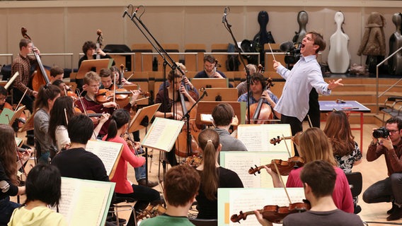 Ein Dirigent macht wilde Bewegungen vor dem Orchester.  Foto: Marcus Krüger