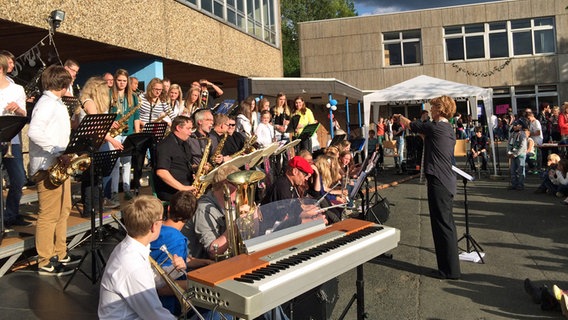 Eine Lehrerein dirigiert eine Schüler-Bigband auf dem Schulhof.  