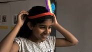 Ein Mädchen setzt sich einen idianischen Federschmuck auf den Kopf.  