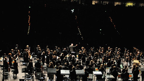 Dirigent und Musiker beim Schlussapplaus vor den dunklen Rängen des Zuschauerraums © NDR Foto: Marco Maas