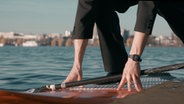 Ein Mann in Anzug (Fabian Diederichs, NDR Elbphilharmonie Orchester) steigt auf ein SUP-Board an der Außenalster. © NDR 