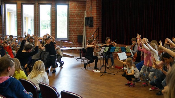 Szene aus einem Schulkonzert: Kinder mit ausgestreckten Armen vor einem Streichquartett.  Foto: Wito Gasthaus