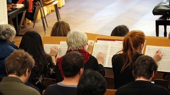 Blick von hinten über die Reihen der Choristen. Es werden eifrig Eintragungen ins Notenmaterial vorgenommen. © NDR Foto: Chantal Nastasi