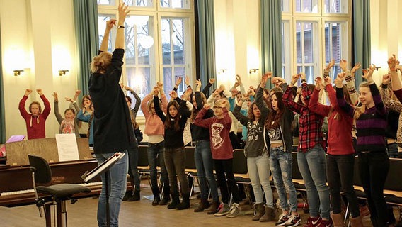 Chorleiterin streckt Arme in die Höhe, Mädchen tun es ihr nach. © NDR Foto: Kristien Daled