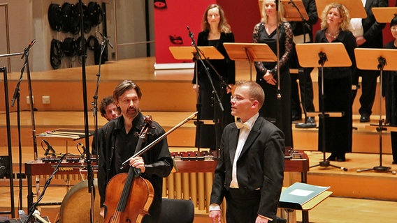 Konzertszene: Cellist Ivan Monighetti, Dirigent Philipp Ahmann und Chorsängerinnen beim Applaus © NDR Foto: Kristien Daled