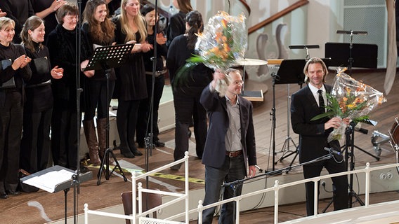 Dirigent Eric Whitacre und Einstudierer Cornelius Trantow winken beim Schlussapplaus mit Blumensträußen. © NDR Foto: Dirk Uhlenbrock