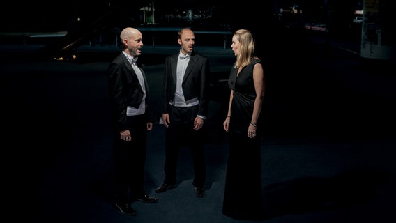 David Csizmár, Andreas Heinemeyer und Anna-Maria Torkel vom NDR Vokalensemble in Konzertkleidung in städtischer Umgebung © NDR Foto: Anderas Rehmann