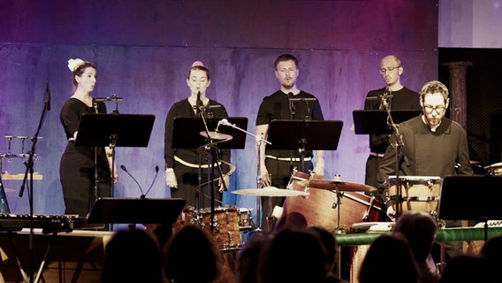 Screenshot: Mitglieder des NDR Vokalensembles singen in der Halle 424 in Hamburg - mit dabei: Elbtonal Percussion. © NDR Vokalensemble Foto: Screenshot