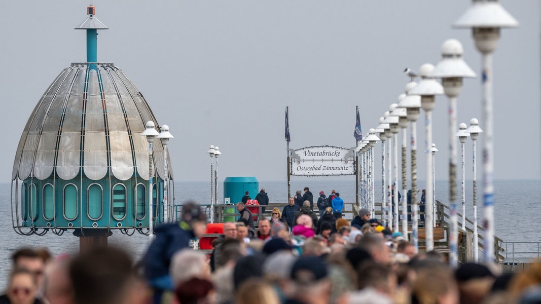 Touristen sind bei sonnigem Wetter im Ostseebad Zinnowitz auf der Seebrücke am Strand unterwegs.