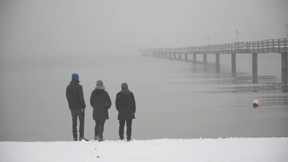 Drei Personen stehen am Ostseestrand. © NDR 