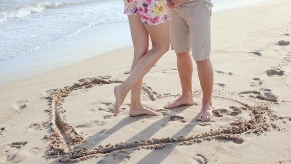 Ein Paar steht in einem in den Sand gemalten Herz. © rasstock/fotolia Foto: rasstock