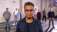 Michail Paweletz steht in einer Halle. Hinter ihm stehen weitere Personen. © NDR 
