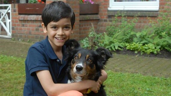 Luis sitzt im Garten und umarmt einen Hund © NDR/Studio Hamburg Foto: Romano Ruhnau